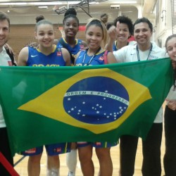 Imagem: Professor do curso de Educação Física juntamente com o time de basquete feminino sub-19 e Comissão técnica segurando a bandeira do Brasil